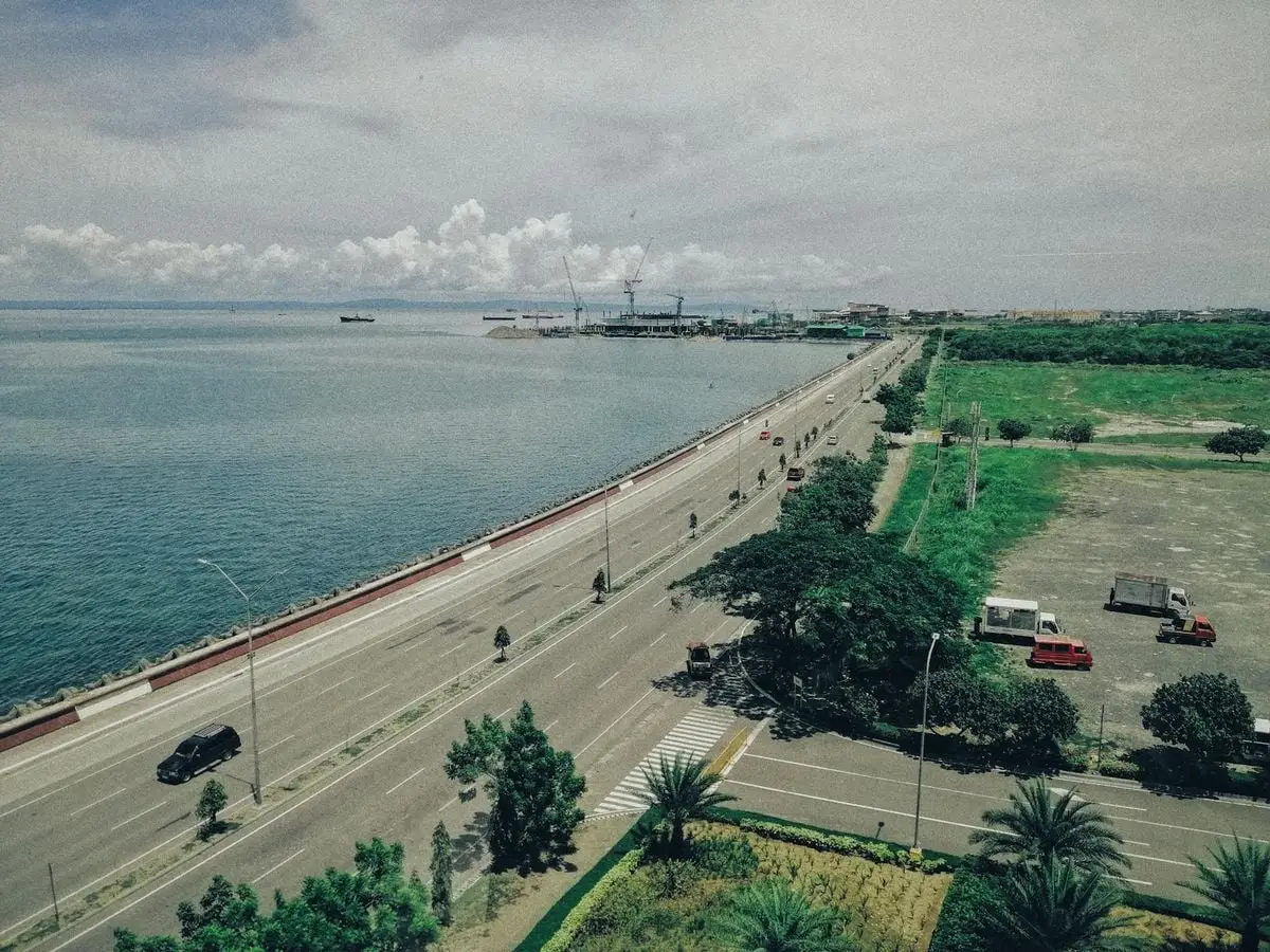 Aerial view of a coastal highway beside a sea shore with visible parking area and greenery.
