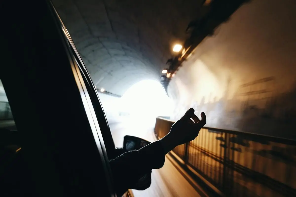A hand extends out of a car window while driving through a brightly lit tunnel.
