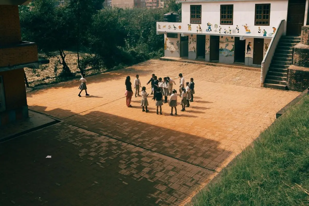 Group of children playing together on a sunny day in a school yard with murals outside.