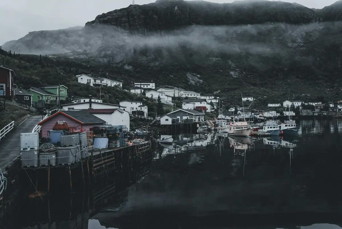 Misty harbor with fishing boats in a serene fishing village, framed by fog and hills.