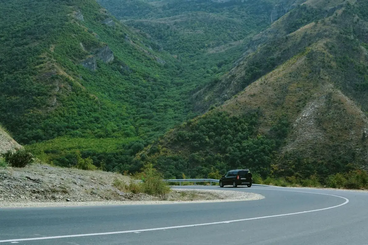 A black car navigating a winding road through lush green mountains, perfect for travel themes.