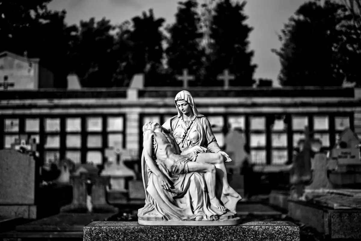 A solemn black and white depiction of the Pietà statue in a Madrid cemetery.