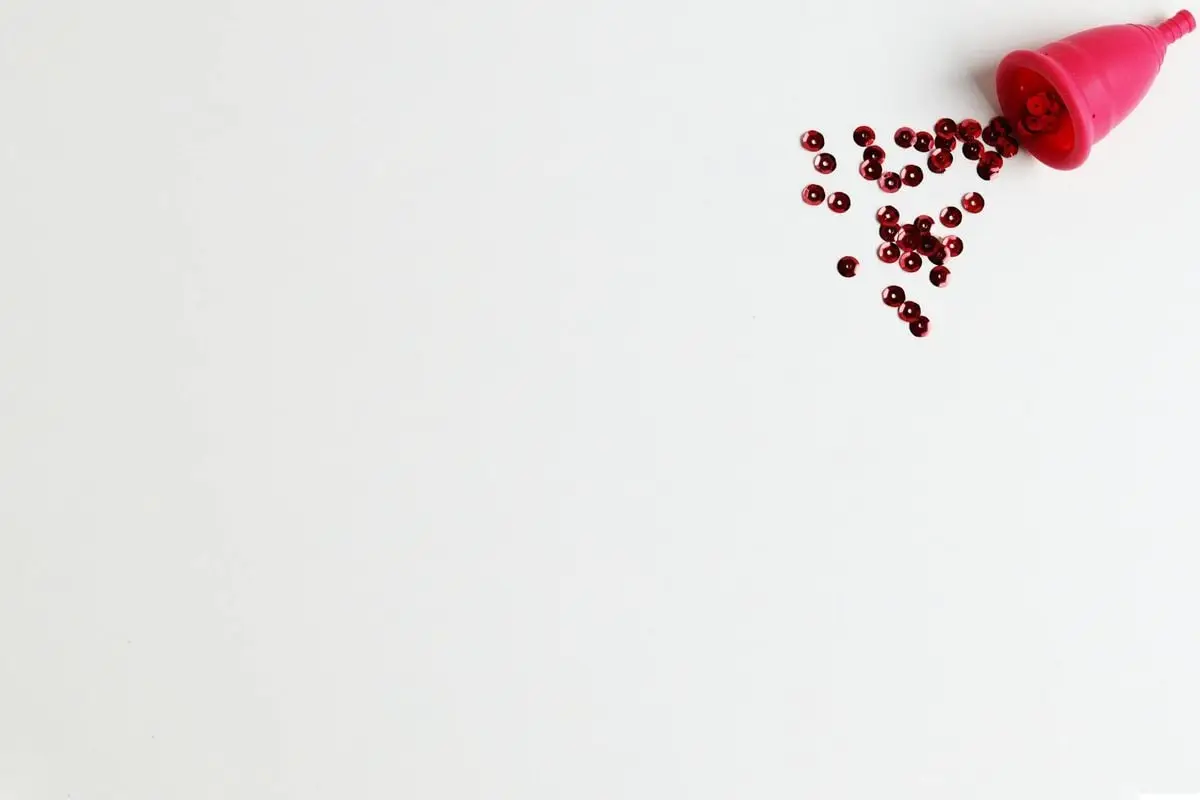 Pink menstrual cup with scattered red beads on a white background, symbolizing menstruation.