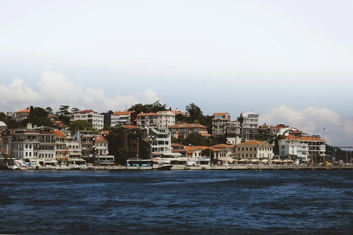 Picturesque coastal town with a harbor, featuring docked boats and charming waterfront buildings under a clear sky.