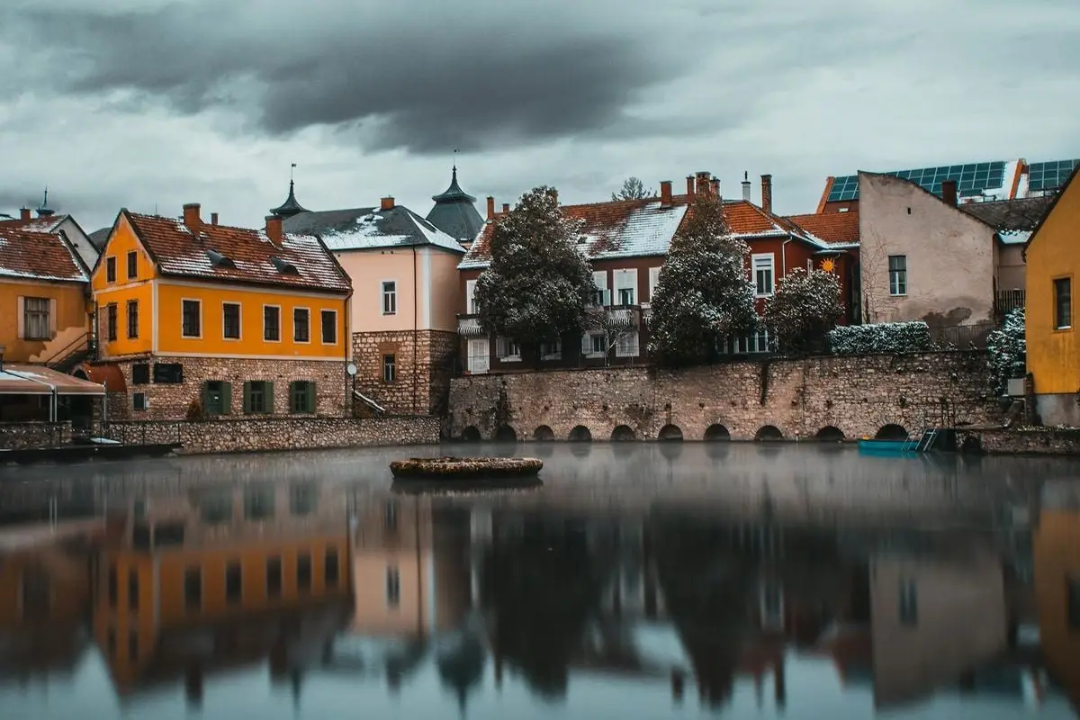 Picturesque view of Tapolca Hungary reflecting on tranquil waters under cloudy skies.
