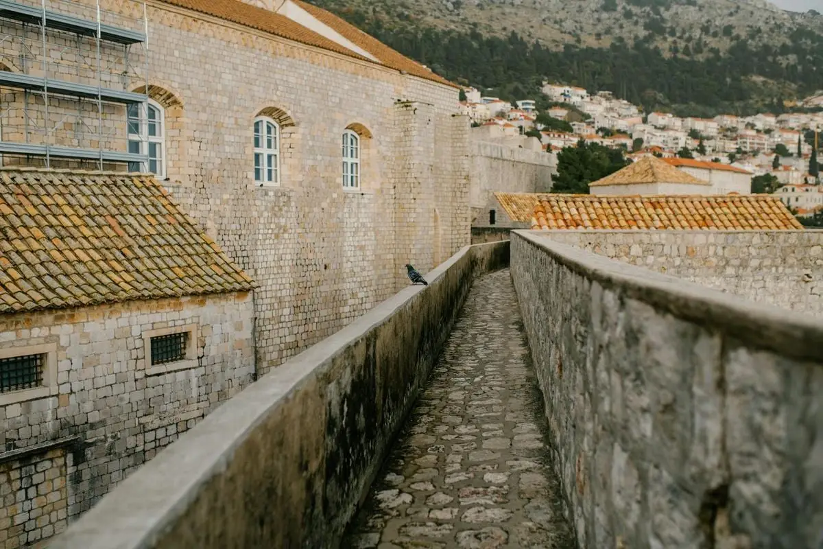 A scenic view of the ancient stone walls in Dubrovnik with a narrow cobblestone walkway.