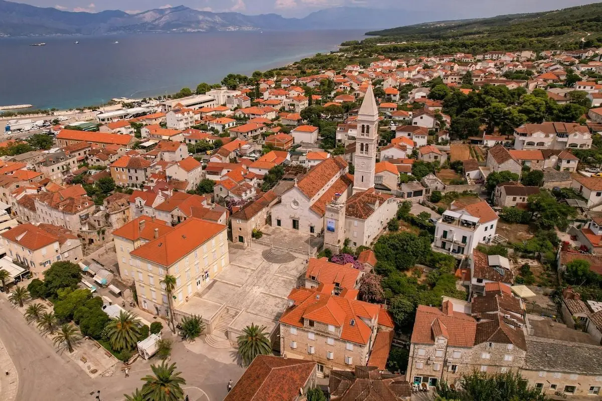 Scenic aerial view of a charming Croatian town by the sea with recognizable church and red-roofed buildings.