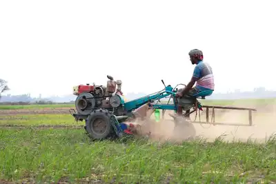 A farmer working a tractor in a green field during the day in Pabna, Bangladesh.