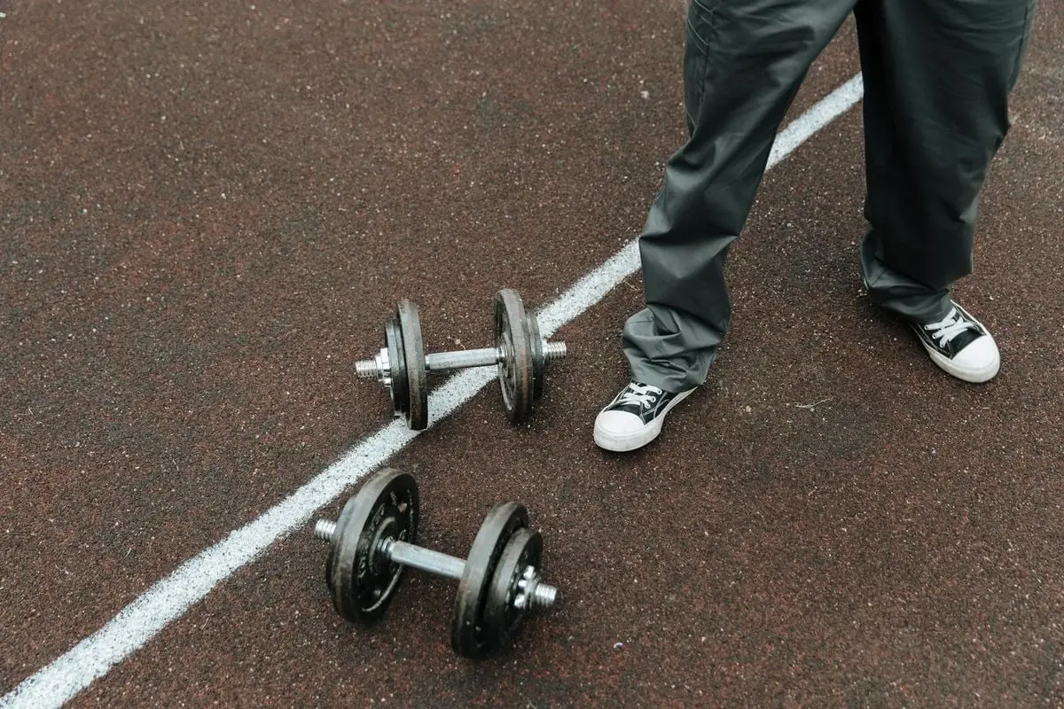 Dumbbells on an outdoor sports track with a person in casual wear.