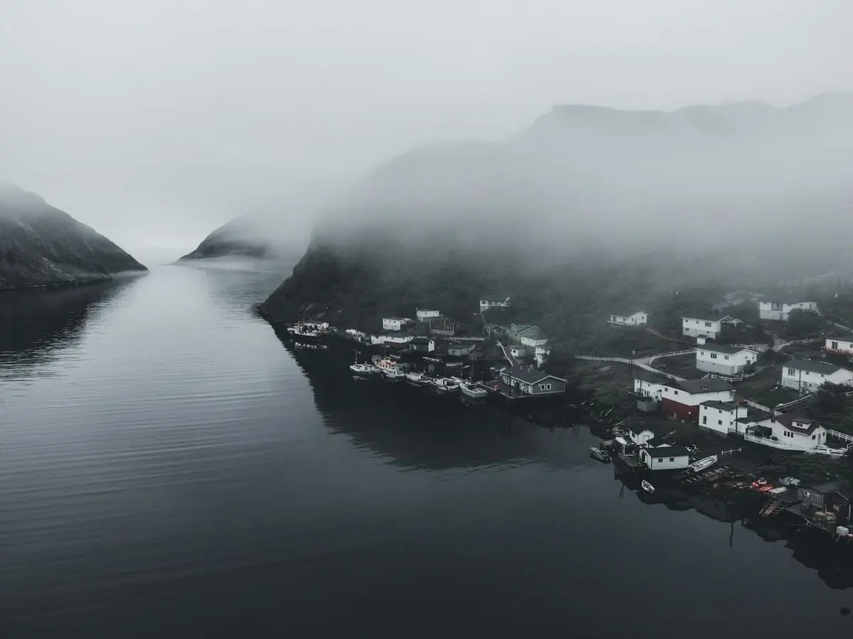 A serene coastal town shrouded in mist and fog with surrounding hills reflecting in the calm water.