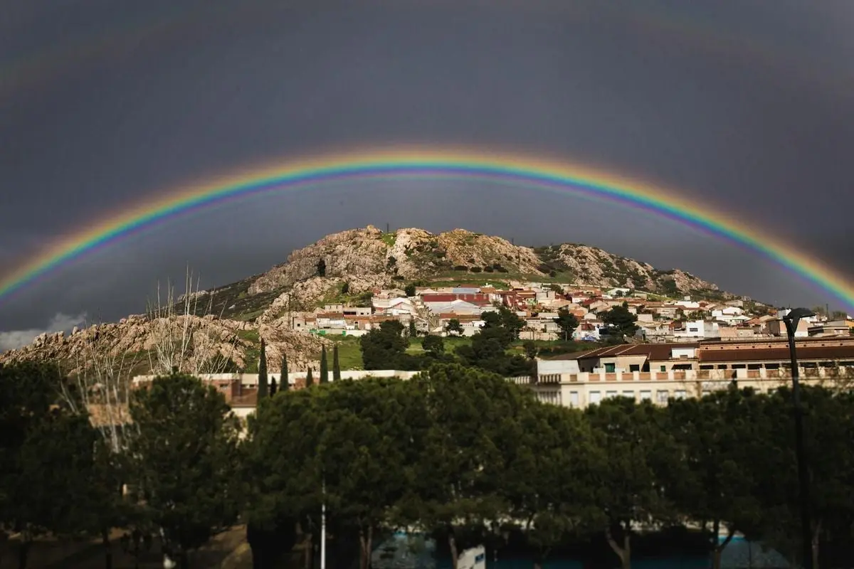 Vibrant rainbow arches over a picturesque hillside town, capturing a moment of natural beauty.