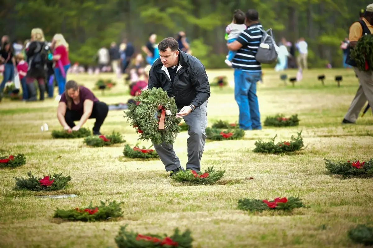 People placing wreaths on graves during a memorial ceremony in a cemetery.