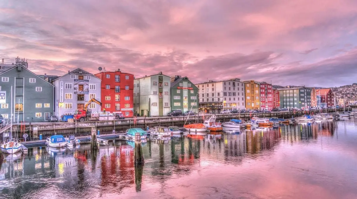 Vibrant waterfront scene of Trondheim, Norway at sunset with colorful buildings and calm water reflections.
