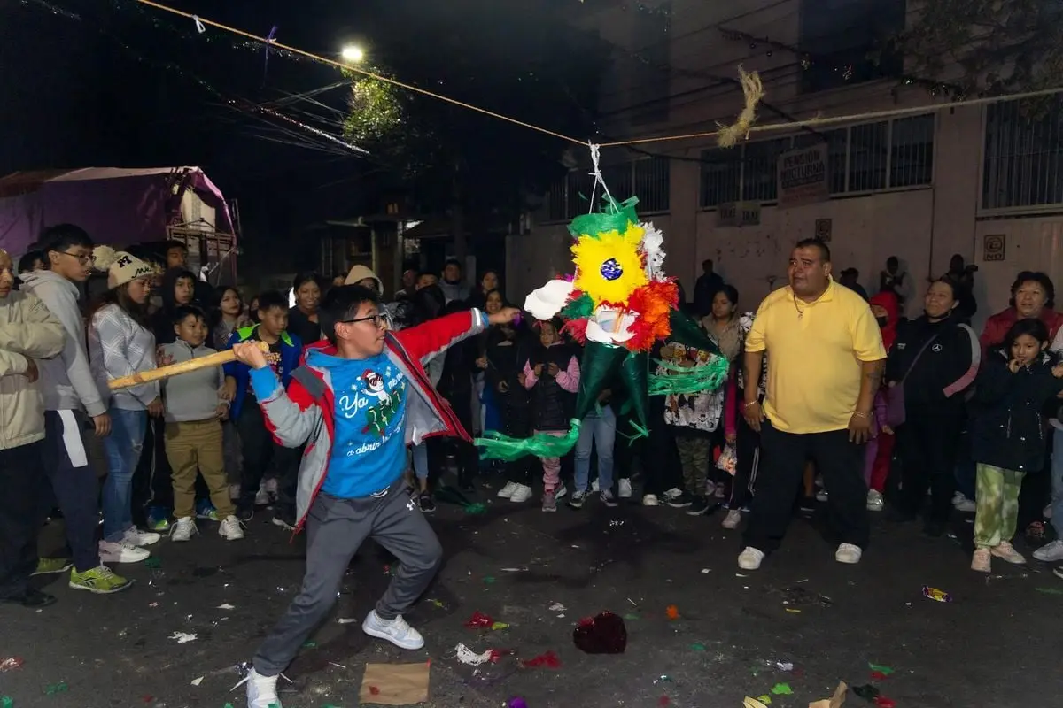 Lively night street scene in Coyoacán, CDMX, with children breaking a colorful piñata.