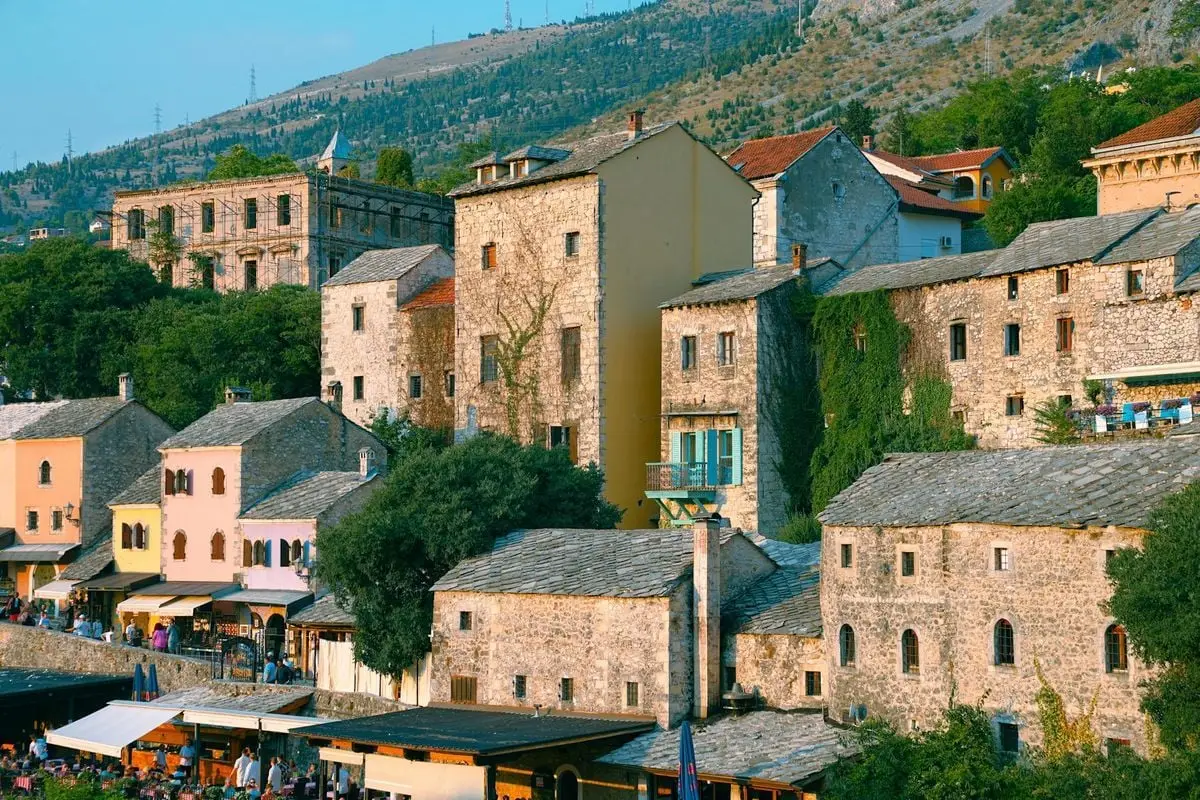 Explore the rustic charm of Mostar's historic stone buildings under a summer sky.