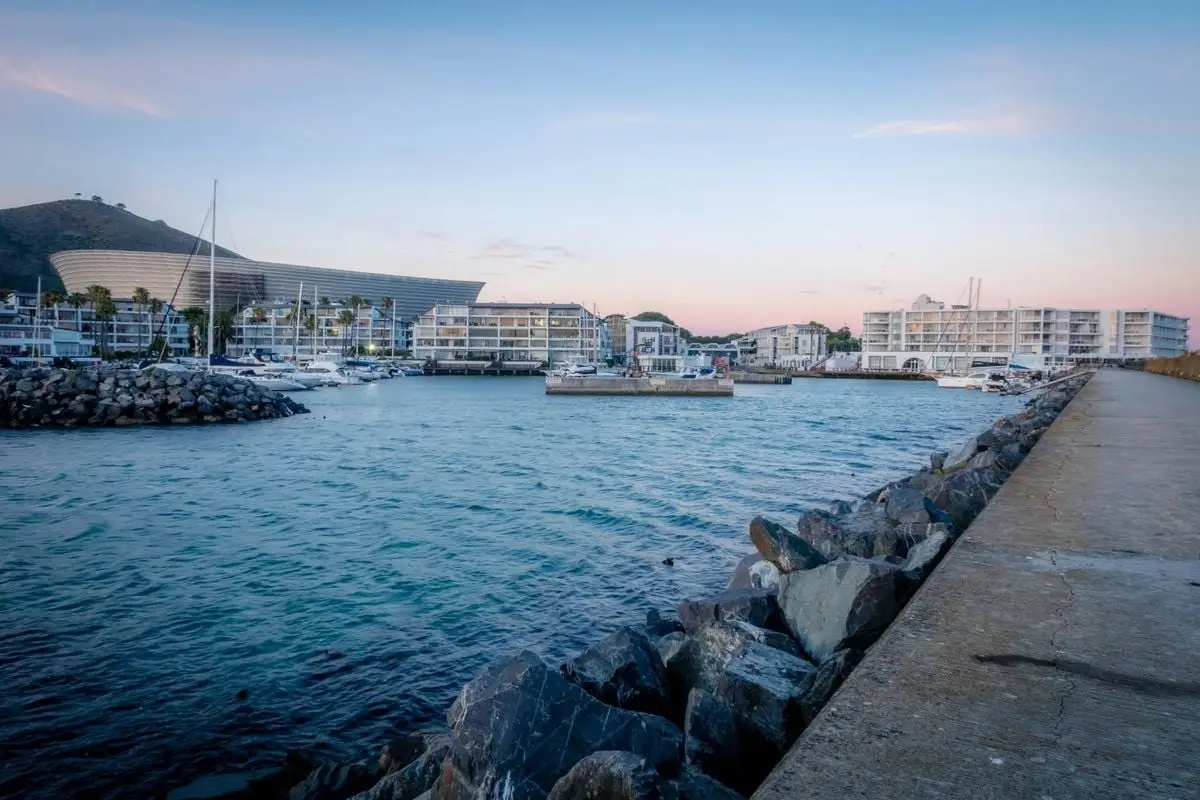 Scenic view of Cape Town's waterfront with yachts and modern buildings during a beautiful sunset.