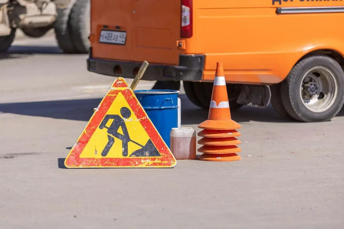 Traffic safety equipment and roadwork sign on an asphalt road near an orange vehicle.