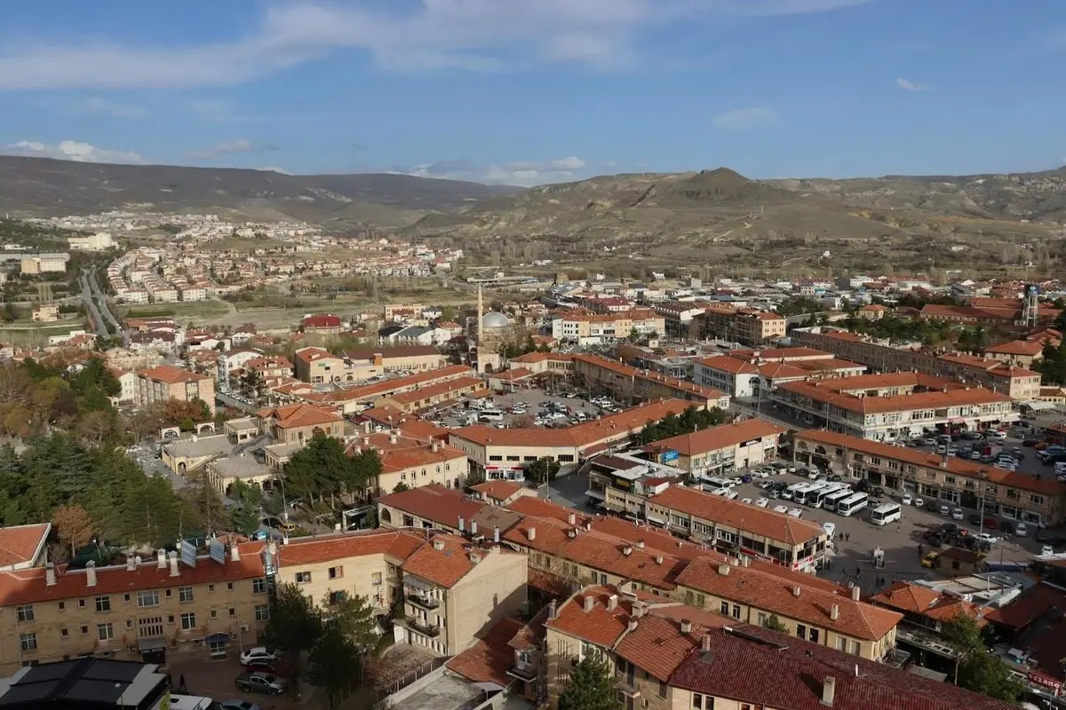 Aerial view of a picturesque town in Cappadocia, Turkey, showcasing red rooftops and surrounding hills under a clear sky.