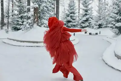 A graceful ice skater in red spins on an outdoor rink, surrounded by snow-covered trees.