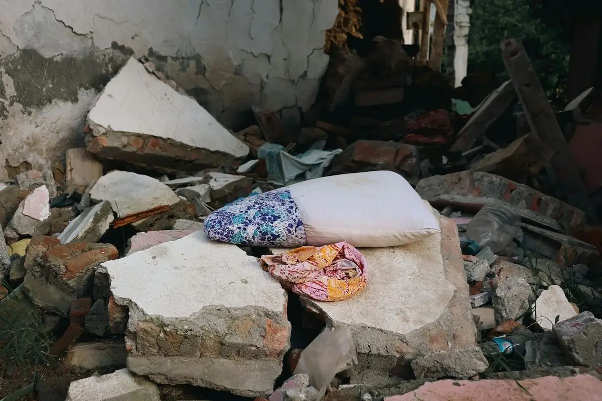 Urban earthquake aftermath showing destroyed buildings, rubble, and a pillow amidst debris, conveying devastation.