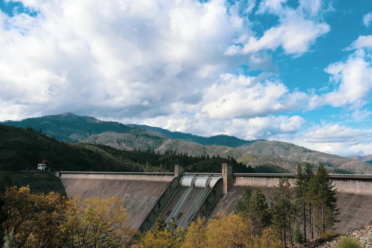 Dramatic landscape of a dam surrounded by mountains under a cloudy sky.
