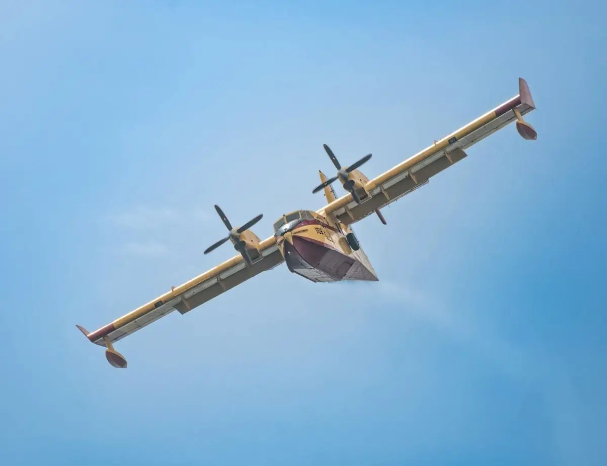 A water bomber airplane flying against a clear blue sky, captured in an aerial shot.