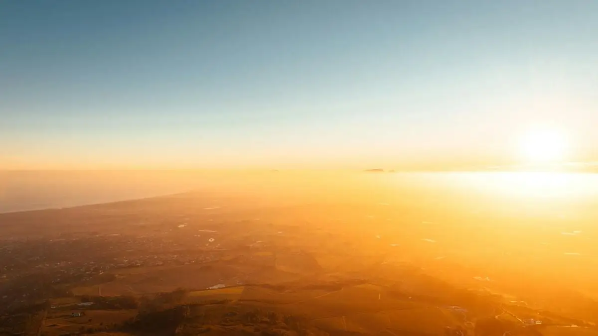 A breathtaking aerial view of Cape Town's landscape at sunrise, with golden hues and a hazy sky.