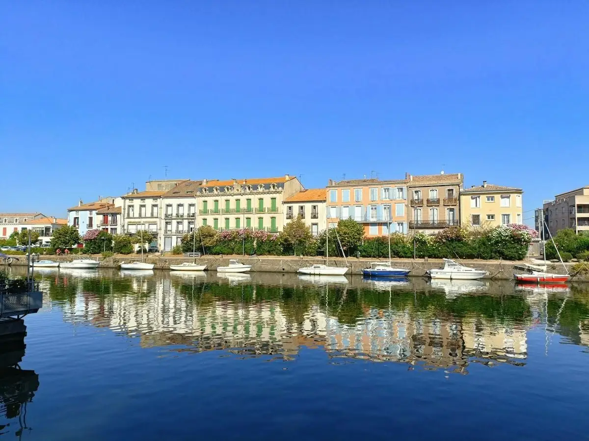 Scenic view of colorful buildings and boats along the waterfront in Agde, France.