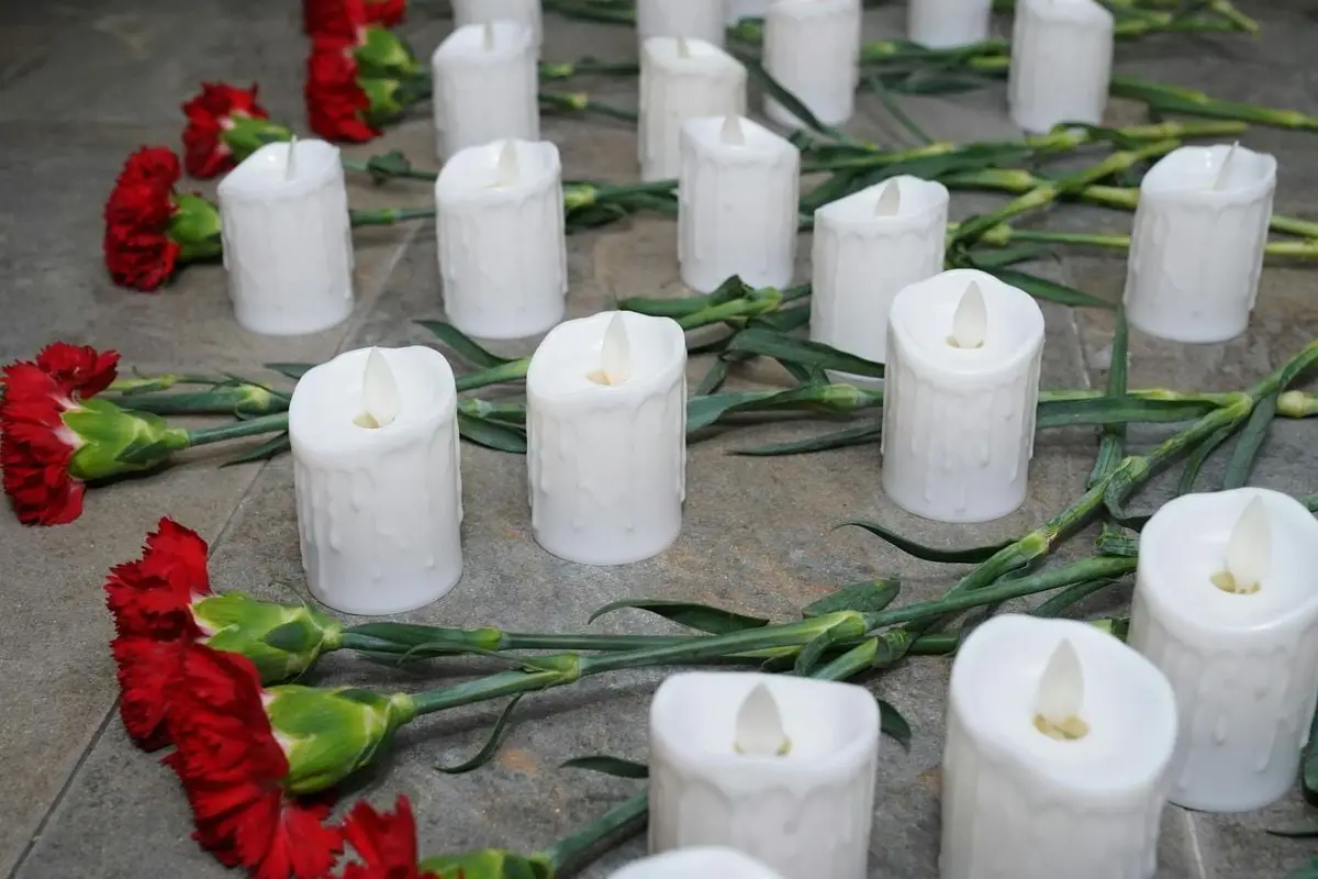 Red carnations and white candles arranged on the floor for a memorial setup.