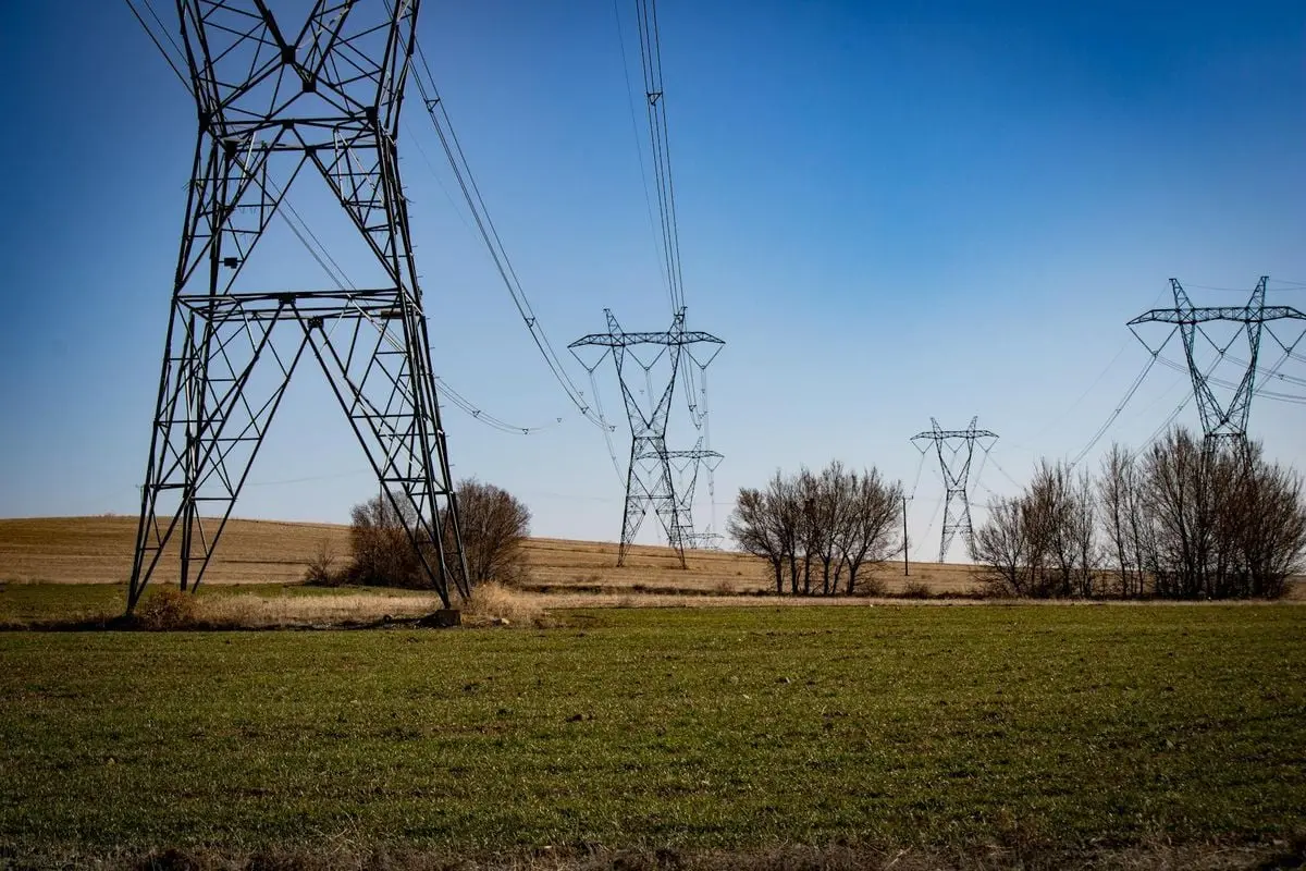 High voltage transmission towers span across an open field under a clear blue sky.