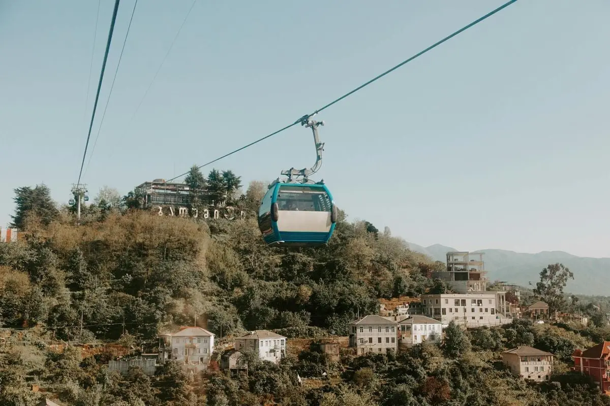 Blue cable car traversing over lush mountains and quaint town buildings.