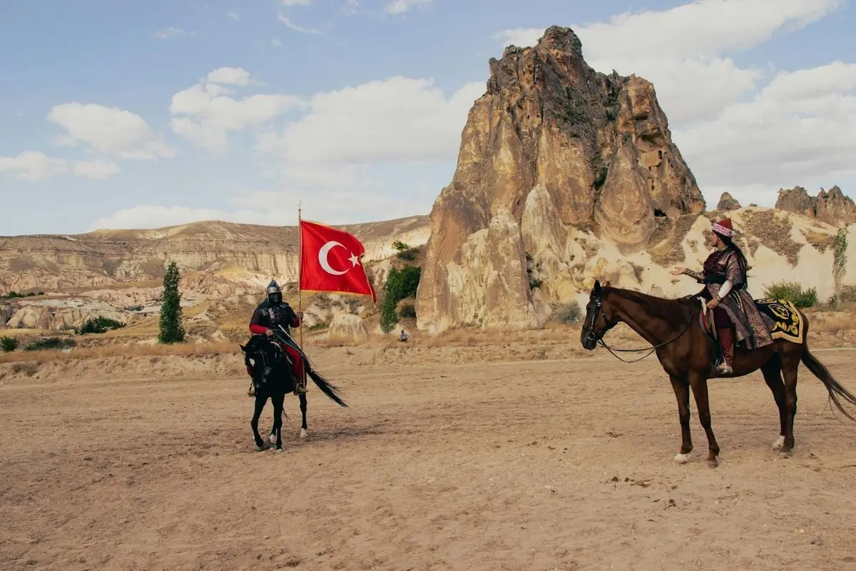 Traditional horsemen with Turkish flag in Cappadocia, showcasing historical culture against rock formations.