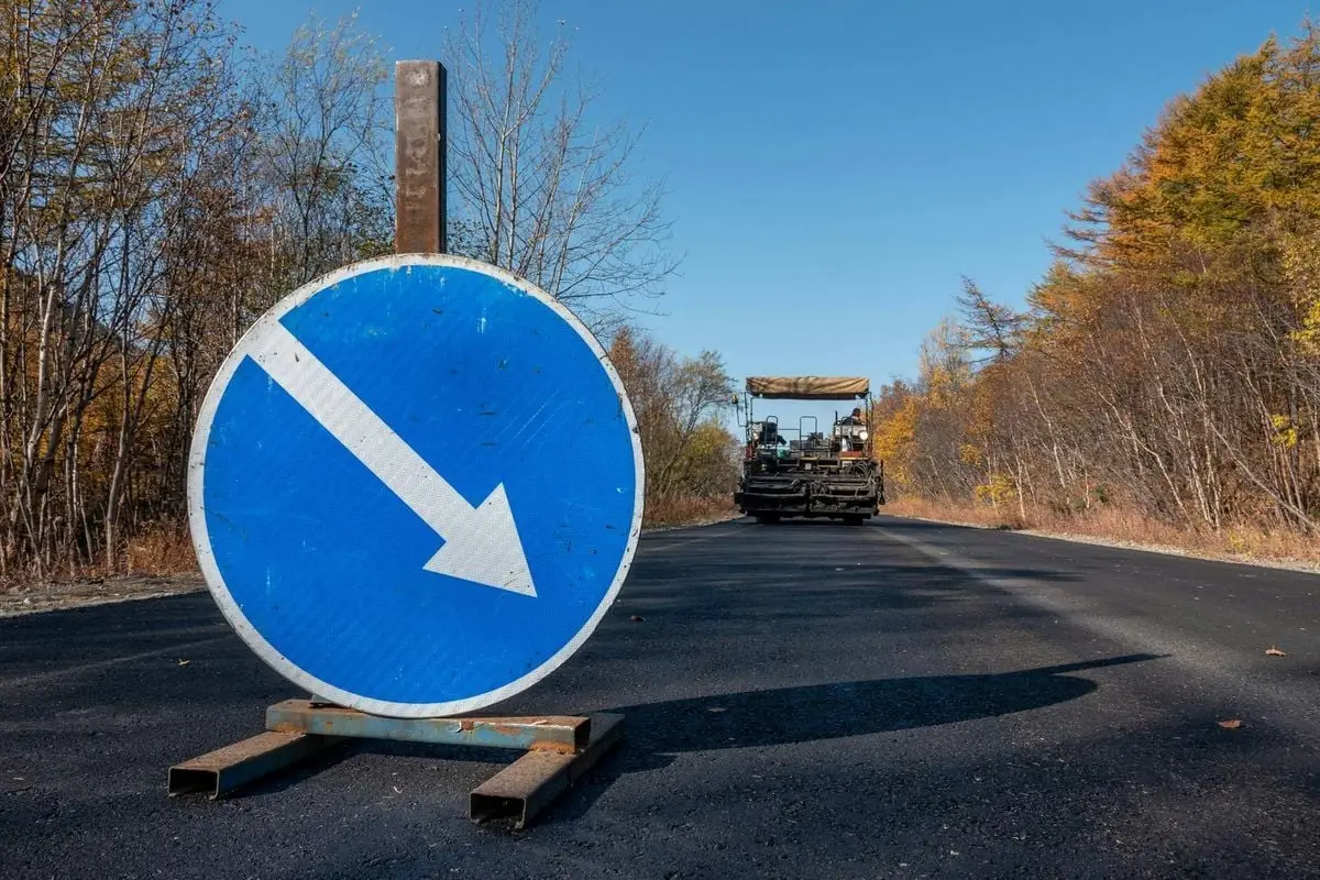 Road construction scene with a blue directional arrow sign on a newly paved road.