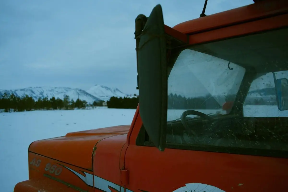 Red vintage truck parked in a snowy field with mountain backdrop, winter setting.