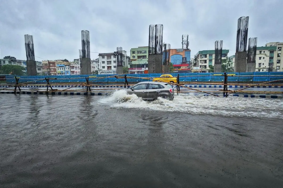 Cars navigate a flooded street in Kolkata, India, under overcast skies.