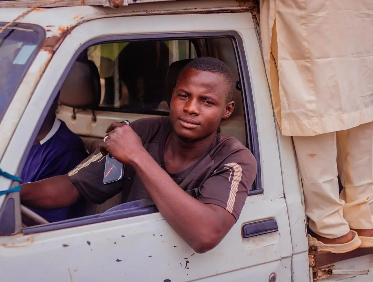 Young man smiling confidently while driving a white truck in an urban area.