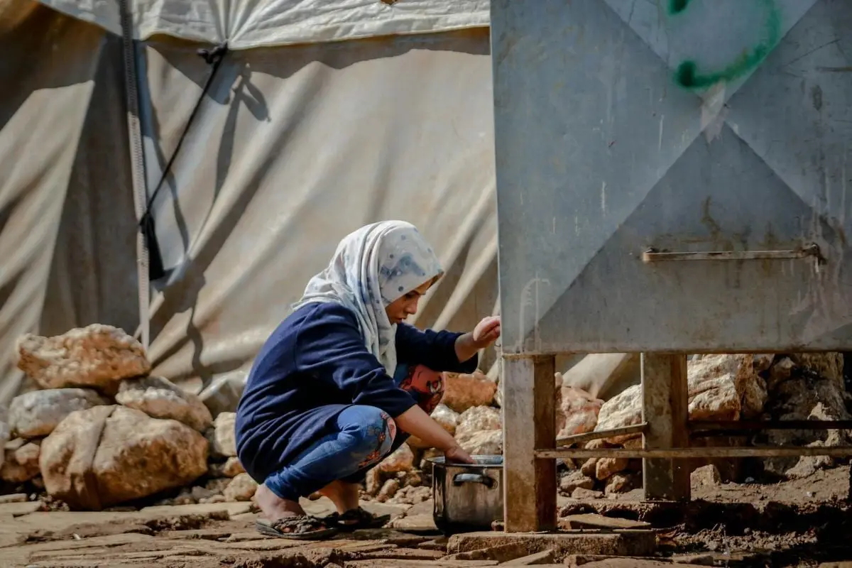 A woman in a hijab collects water in a refugee camp in Idlib, Syria.