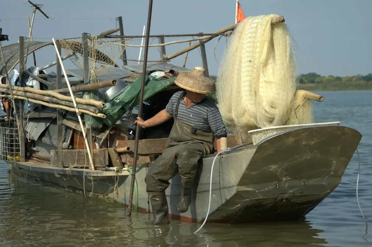 A fisherman on a rustic boat handling fishing nets on a sunny day.