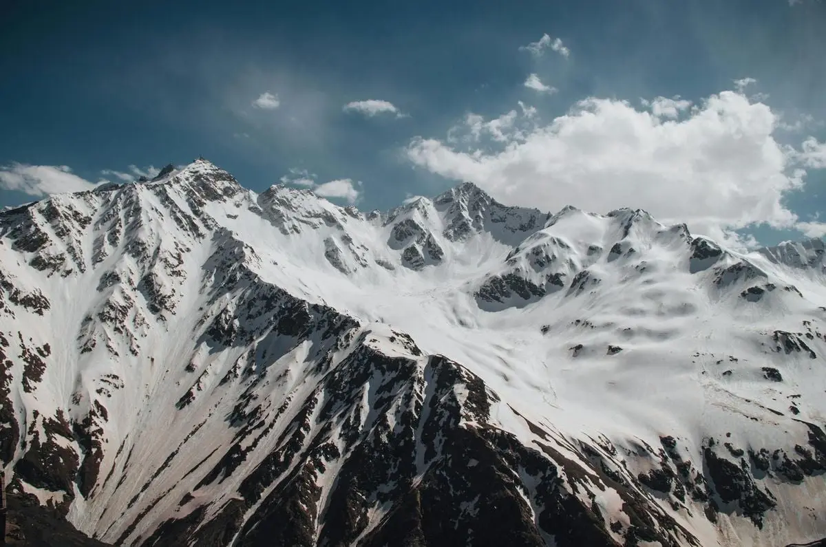 Stunning view of Dombay's snow-covered mountains under a blue sky with white clouds.