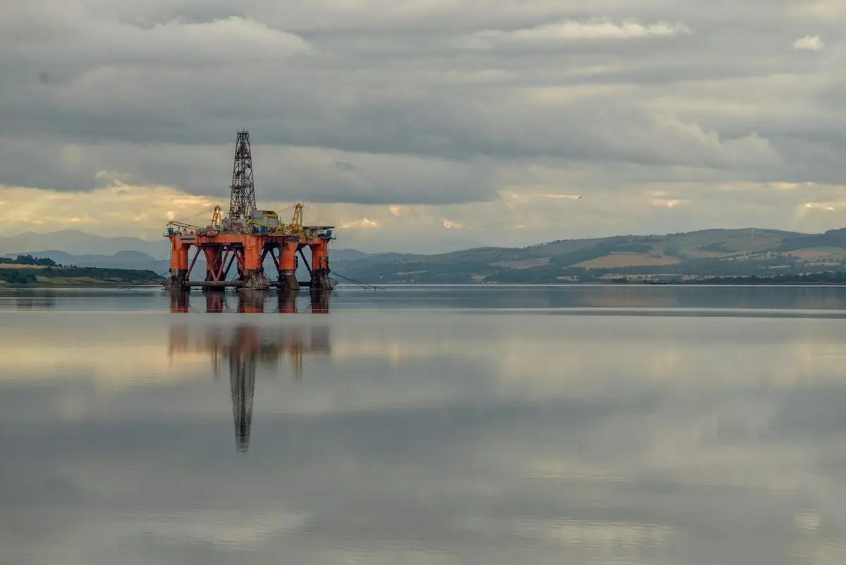 Oil drilling platform reflected on calm sea under stormy clouds in Scotland.