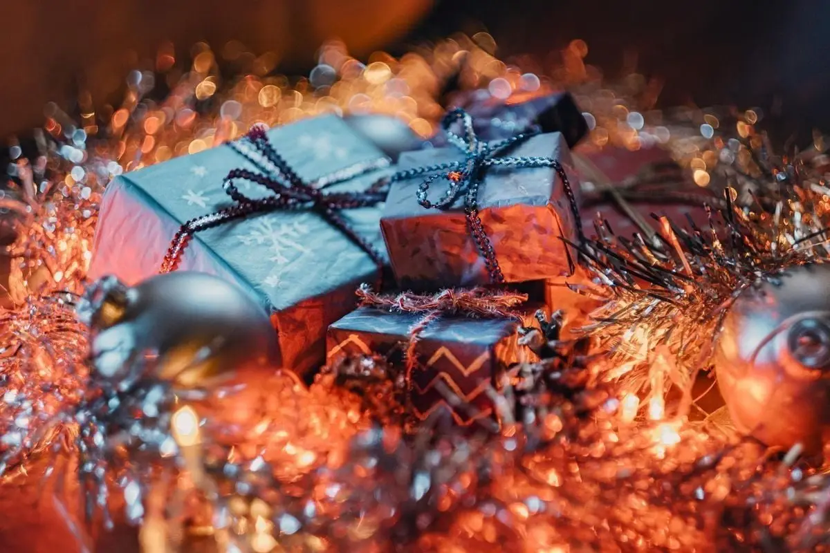 Colorful Christmas gifts nestled among ornaments and tinsel in a warm holiday setting.