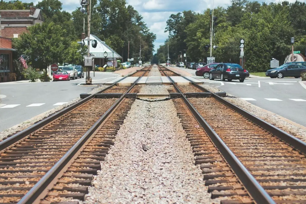 Railroad tracks intersecting through a charming small town with cars and trees.