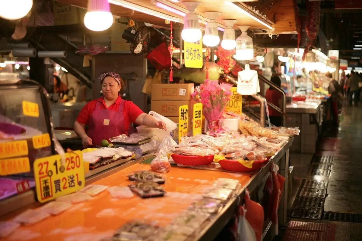 A bustling Asian market scene featuring fresh seafood and vibrant signage with a female vendor.