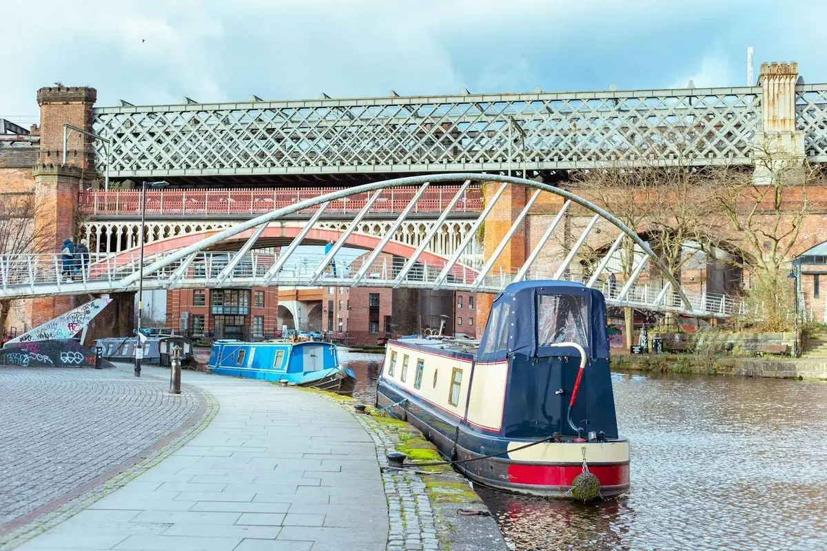 View of canal boats and historic bridges in Manchester, England, showcasing urban architecture.
